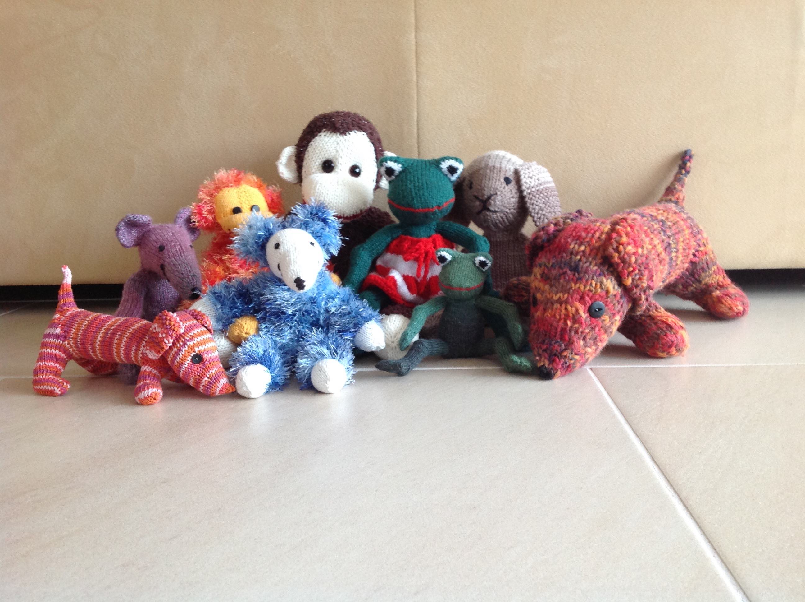 A collection of hand-knitted animals, including various soft toys, displayed together as examples of past knitting projects.