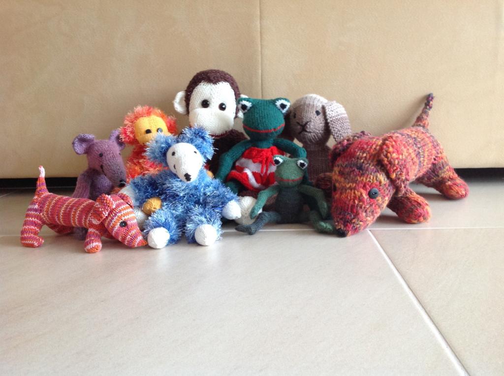 A collection of hand-knitted animals, including various soft toys, displayed together as examples of past knitting projects.